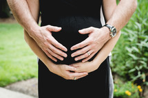 A man and woman's hands on her pregnant belly.