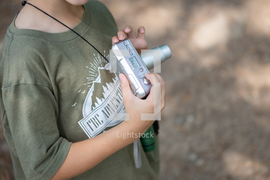 Young boy holding and learning how to use digital camera outside