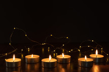 votive candles and string of fairy lights in darkness 