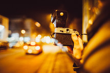 person standing on a city sidewalk at night taking pictures 