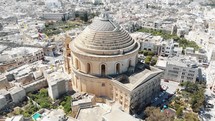 Far view, aerial 4k drone footage, circling the Mosta Rotunda Dome, a Roman Catholic church, and the surrounding city of Malta.