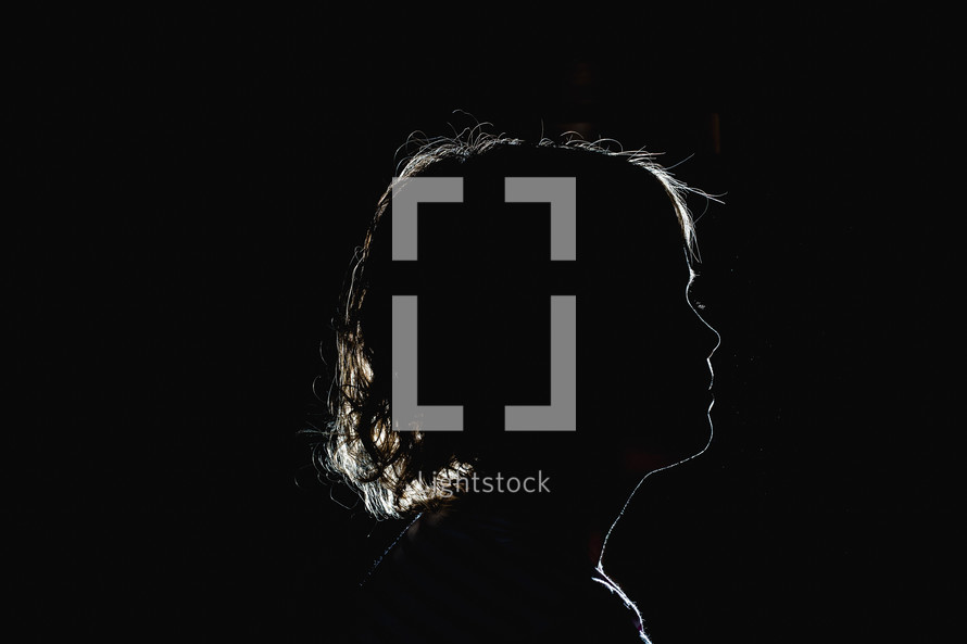 side profile silhouette of a girl child in a dark room 