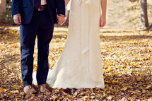 legs of a bride and groom standing in fall leaves 