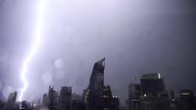 Lightning and rain in modern city center of Bangkok. Storm clouds with lightning strike bolts passing over night city of Bangkok cityscape.