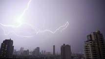 Lightning and rain in modern city center of Bangkok. Storm clouds with lightning strike bolts passing over night city of Bangkok cityscape.