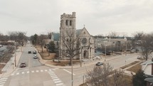 Aerial footage of a cathedral/catholic church on the corner of a street during winter with dead trees