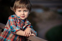 Toddler boy leaning against woodeen rail.