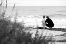 A man and a small boy standing on a beach and looking out at the ocean.