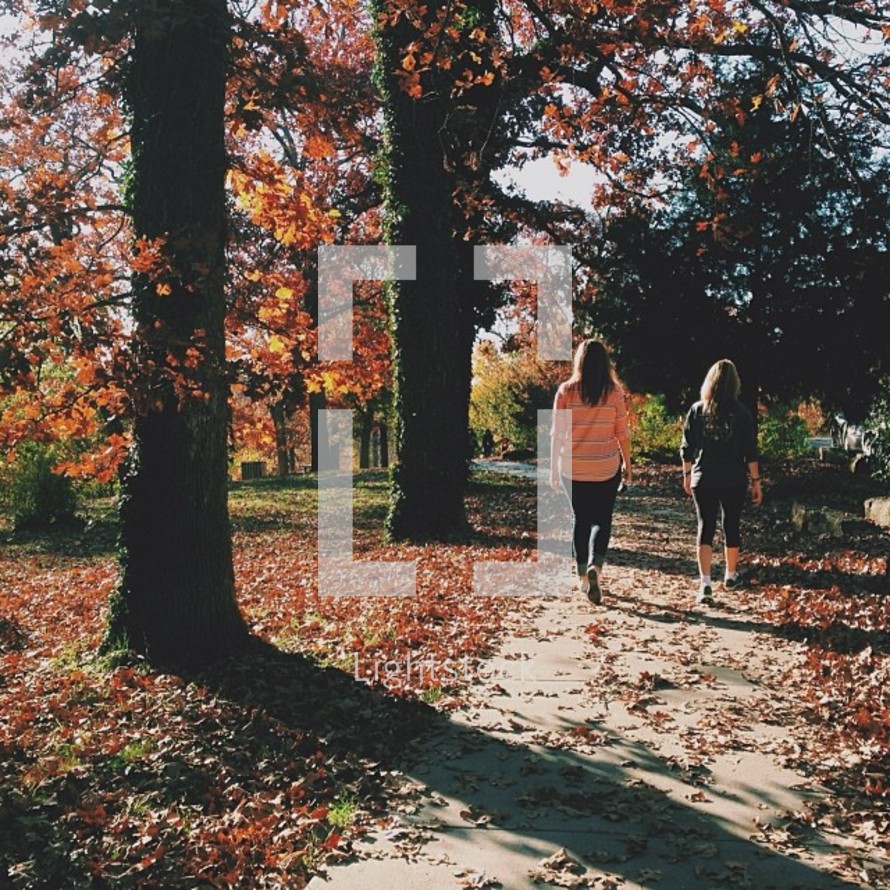 Two women walking along a path through trees.