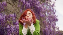 Woman blowing wisteria petals towards the camera.