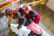 village children gathered around missionary in a classroom 