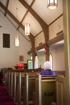 an elderly woman sitting alone in a church praying 
