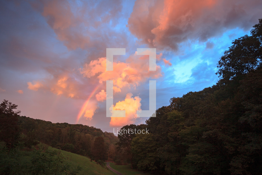Rainbow and bright pink sunset clouds over mountainous forest