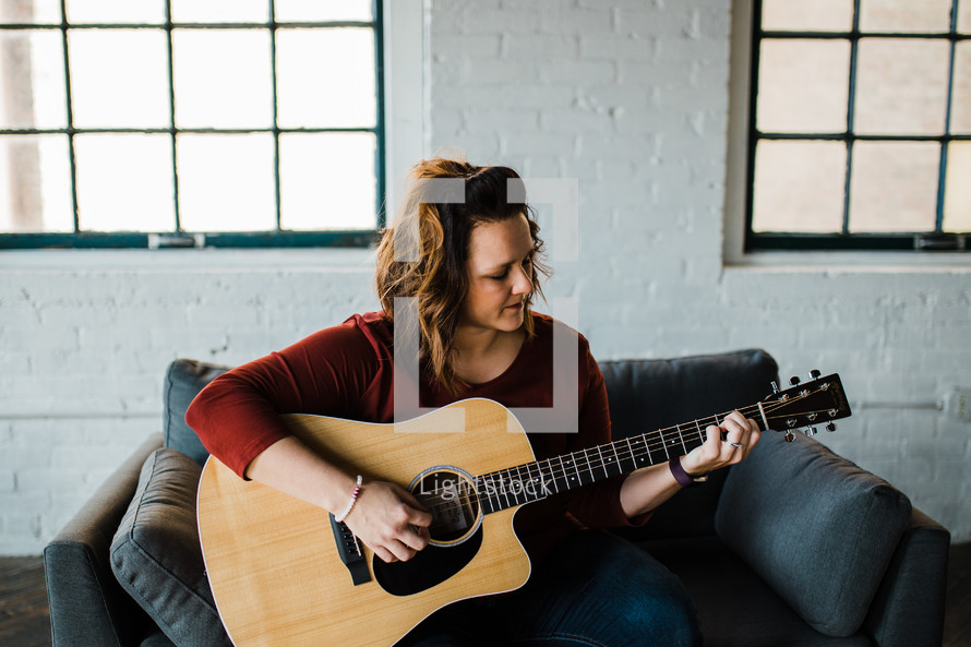 a woman sitting on a couch playing a guitar 