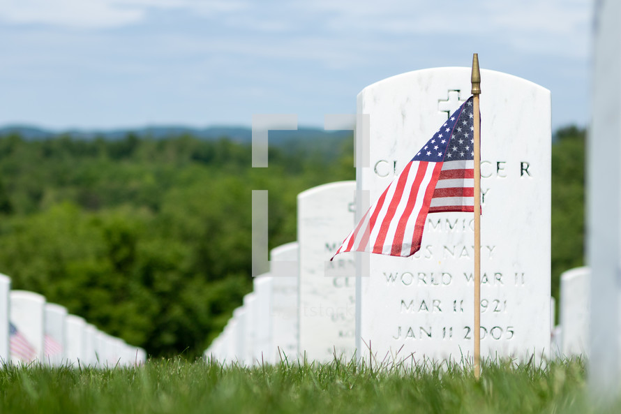 American flag stuck in ground in front of white military gravestone memorials in rural cemetery