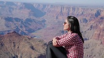 Grand Canyon, Arizona -  tourist woman, sitting on a rock contemplating Grand Canyon scenic view
