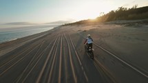 Drone footage of an off-road motorcyclist riding on the shore of a beach at sunset.