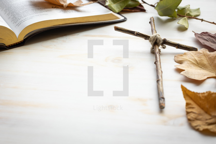 autumn leaves, cross, and Bible on a white wood background 
