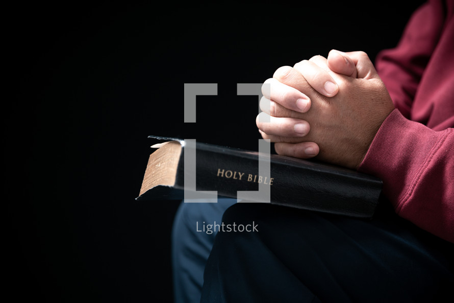 Man folding hands in prayer on on Bible
