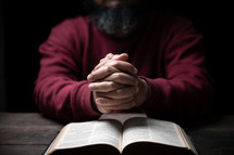 Man's hands folded in prayer over open Bible