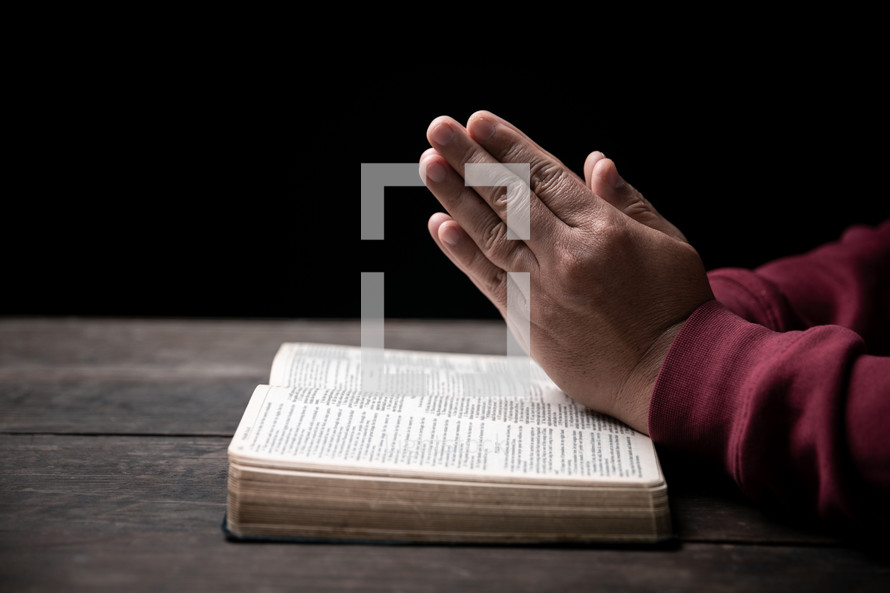 Man's hands folded in prayer over open Bible