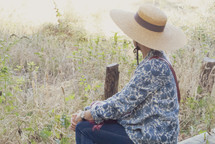 a woman sitting outdoors wearing a hat 
