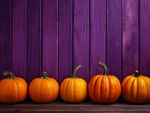 Row of orange pumpkins on purple wooden background. Halloween concept.
