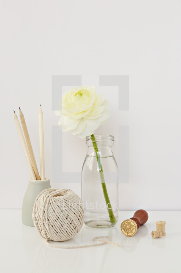 white flower in a clear vase, yarn, stamp, wooden spool 