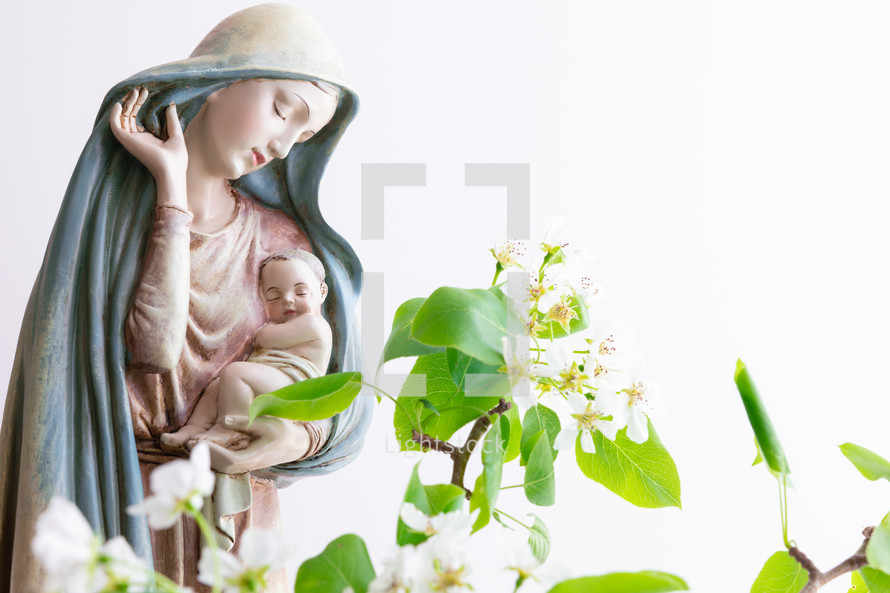 Statue of Mary holding baby Jesus with spring flowers 