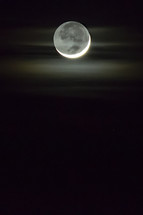 The crescent moon illuminates a small patch of fog in the dark night sky.  
