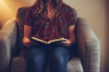 a woman sitting in a chair reading a Bible 