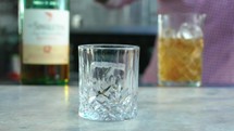 Barman pours big ice cubes into glass in bar closeup. Skilled bartender prepares refreshing cocktail for guest in club. Frozen water for beverage
