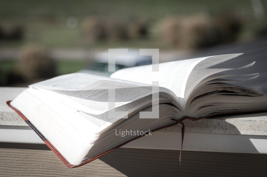 Open Bible on a ledge outside with pages flipping