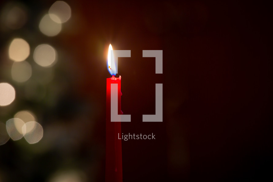 One red melting wax candle burning in front of blurred bokeh Christmas lights