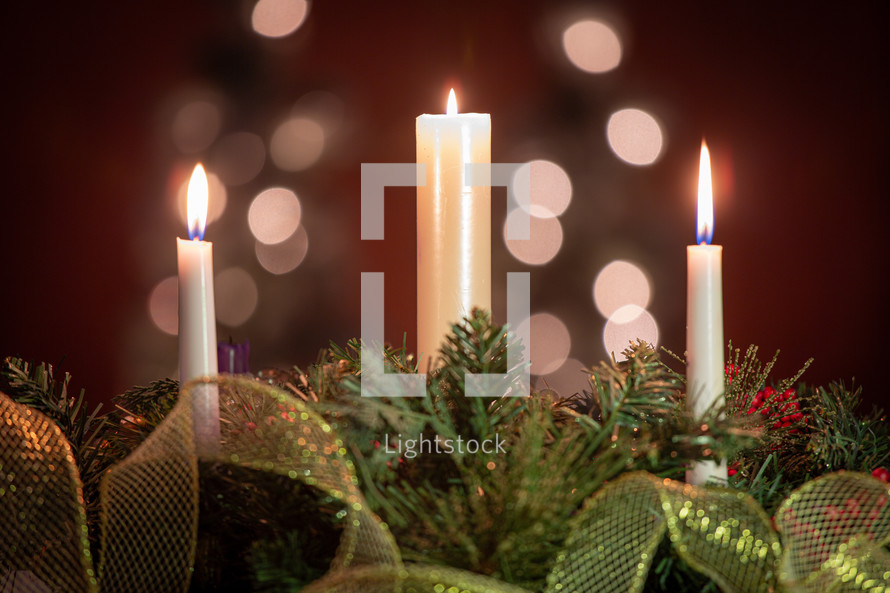 Three burning holiday candles Christmas pine decoration in front of tree bokeh