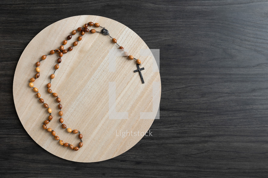 Wood rosary on a light wood round tray on a dark wood background