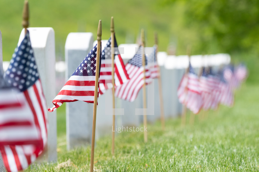 Row of American flags in grass next to gravestone memorials
