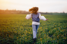 Happy stylish woman running in green field. Young lady in white embroidery shirt. Freedom, summer, love, ethno, folk lifestyle. 