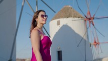 A beautiful tourist woman enjoys the view to the famous windmills on Mykonos island, Greece, during her summer holidays