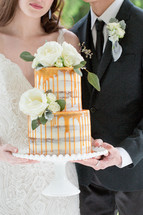 bride and groom holding a wedding cake 