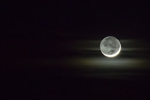 A small patch of fog is illuminated by the a waxing crescent moon in the dark night sky.  