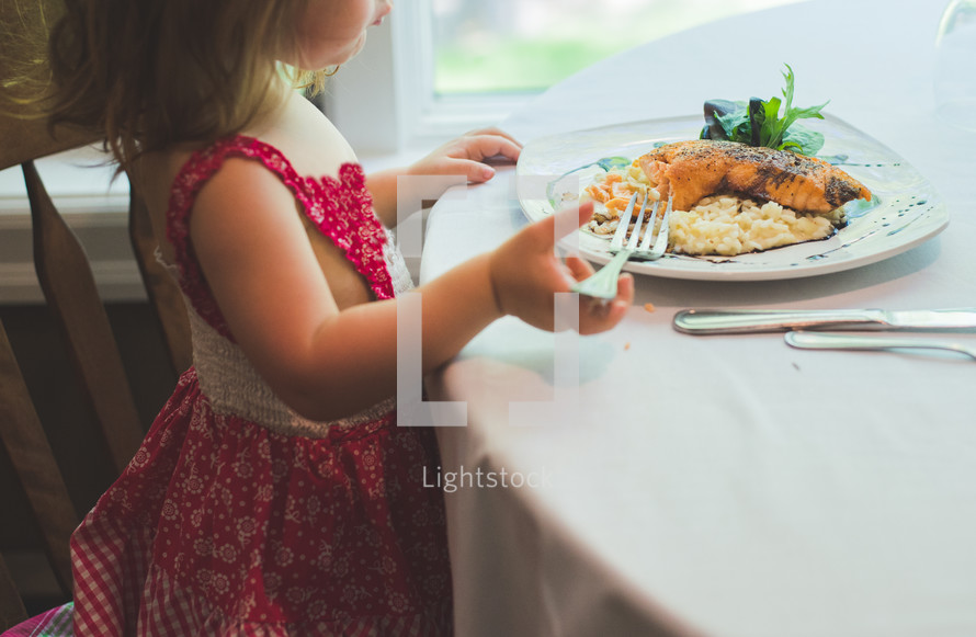 A toddler girl eating dinner at a restaurant.