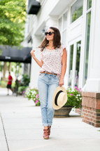 a teen girl holding a hat posing on a sidewalk 