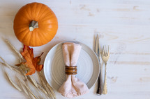 plate and silverware and orange pumpkin on a white wood background 
