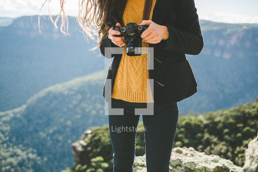 A woman holding a camera on a mountaintop.