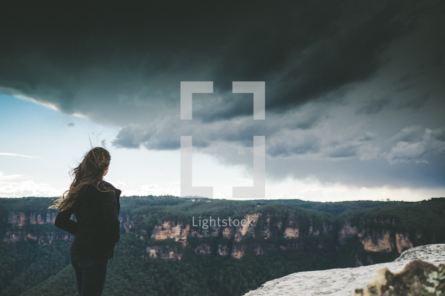 woman standing on a mountain top under a cloudy sky 