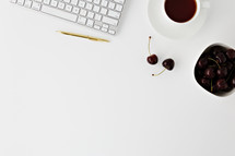 computer keyboard, gold pen, cherries, and coffee cup on white 