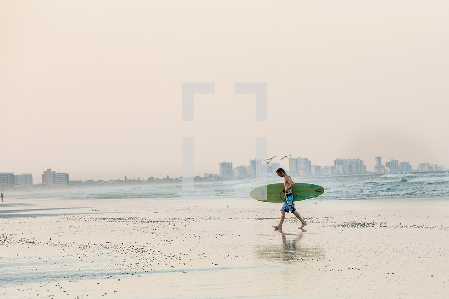 A man carrying a surf board while walking along a beach.
