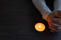 Hands folded in prayer beside a single candle