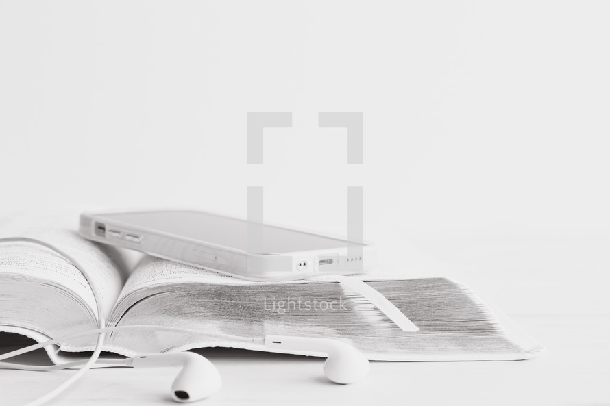 iPhone and earbuds with open Bible on a white wood background 